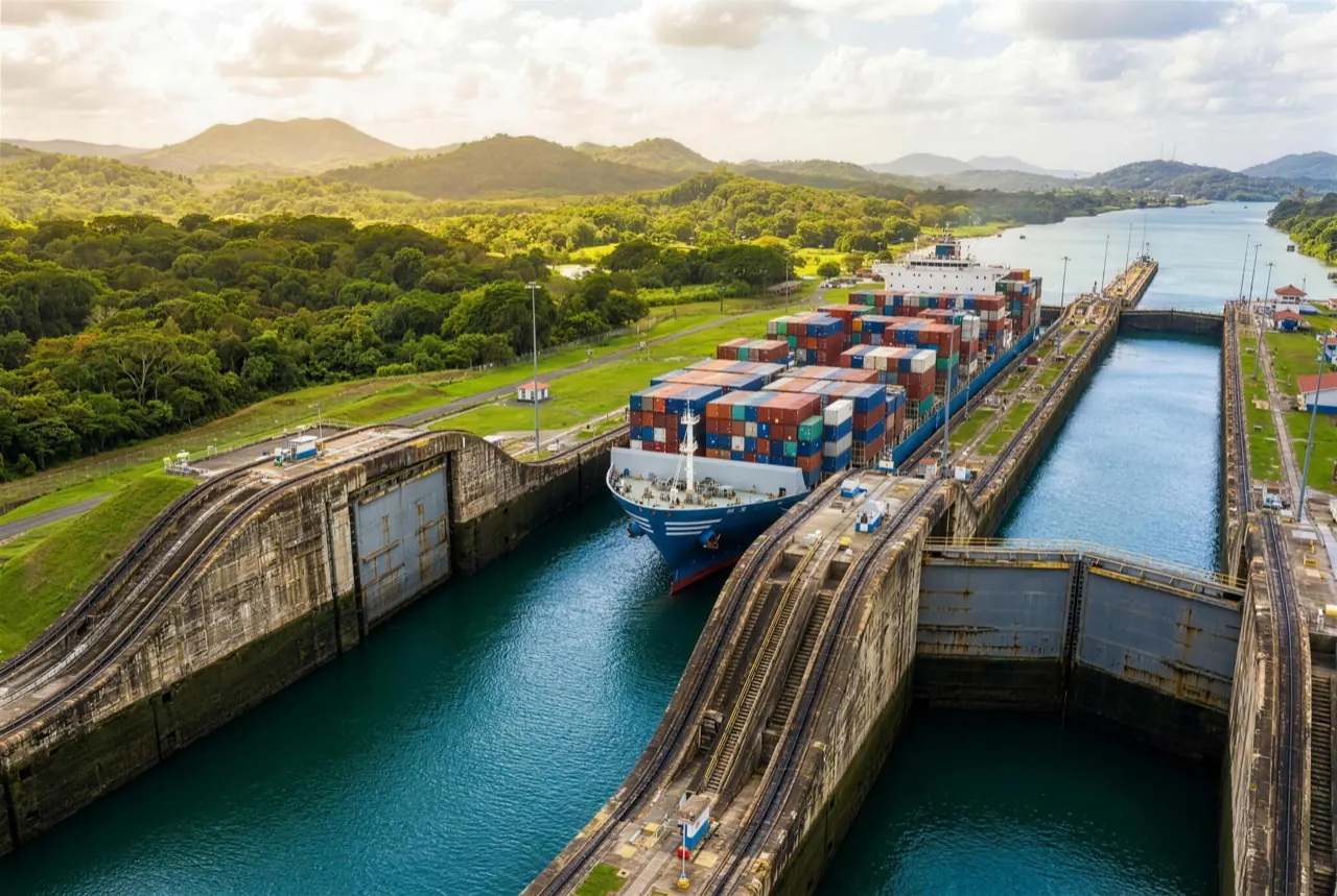 Container ship transiting the Panama Canal locks, framed by tropical rainforest hills, seen from above