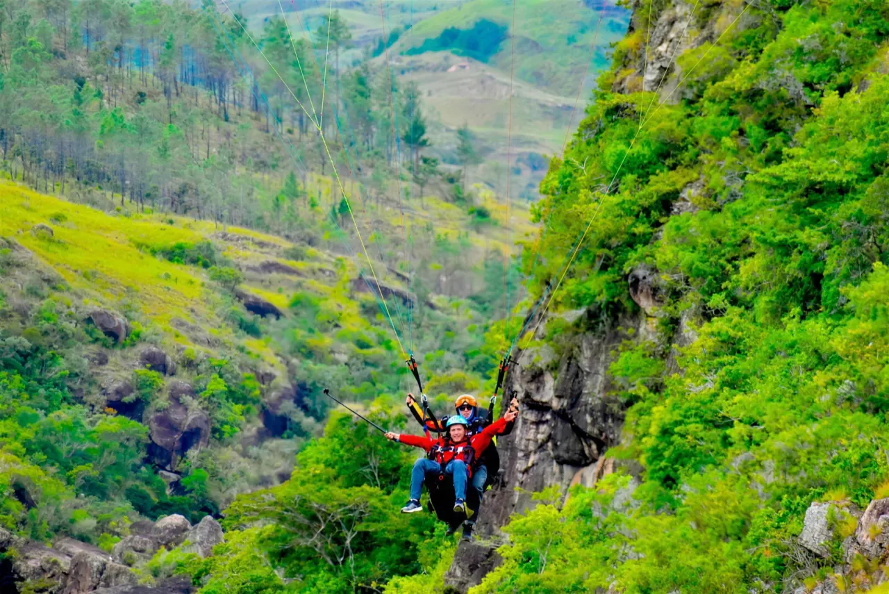 Tandem paraglider soaring over steep green hills and rocky cliffs in the Panama highlands