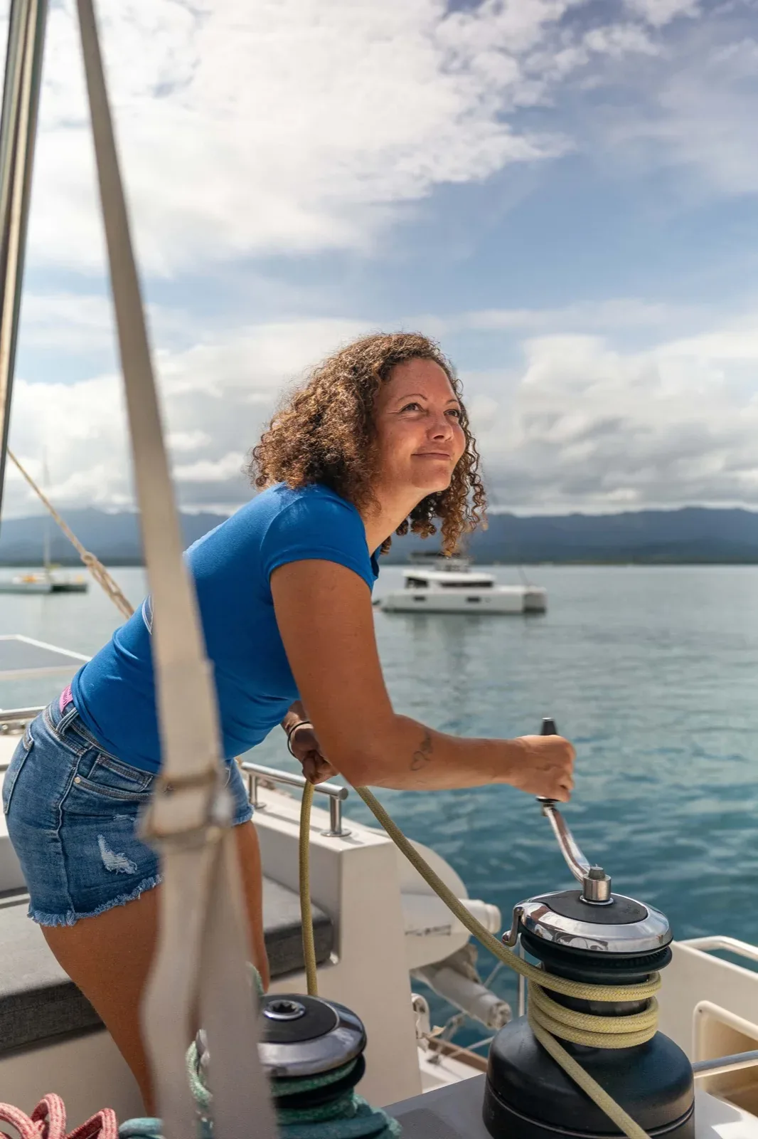 Crew trimming a winch on the side deck of the Lagoon 450, another catamaran anchored behind