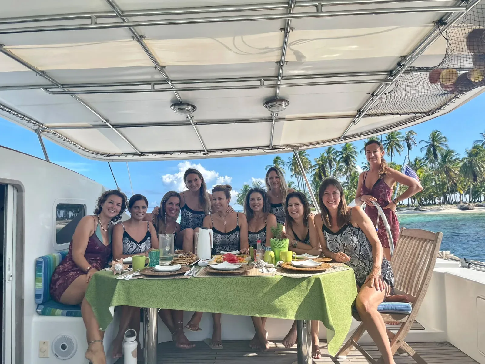 Guests dining under the bimini aboard the Lagoon 55 with a palm island behind