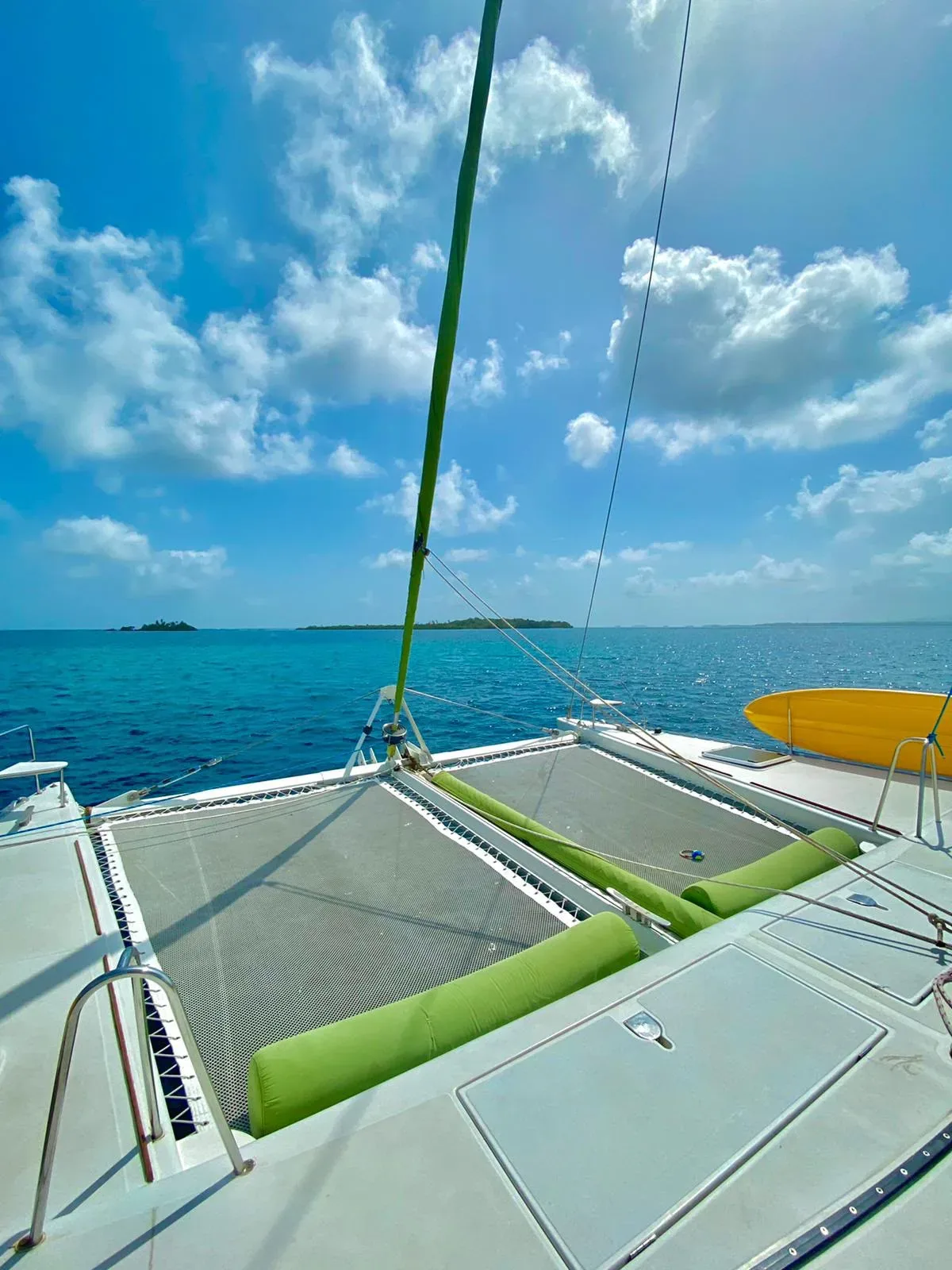 Trampolines and green bolster cushions on the bow of the Lagoon 55, islands on the horizon