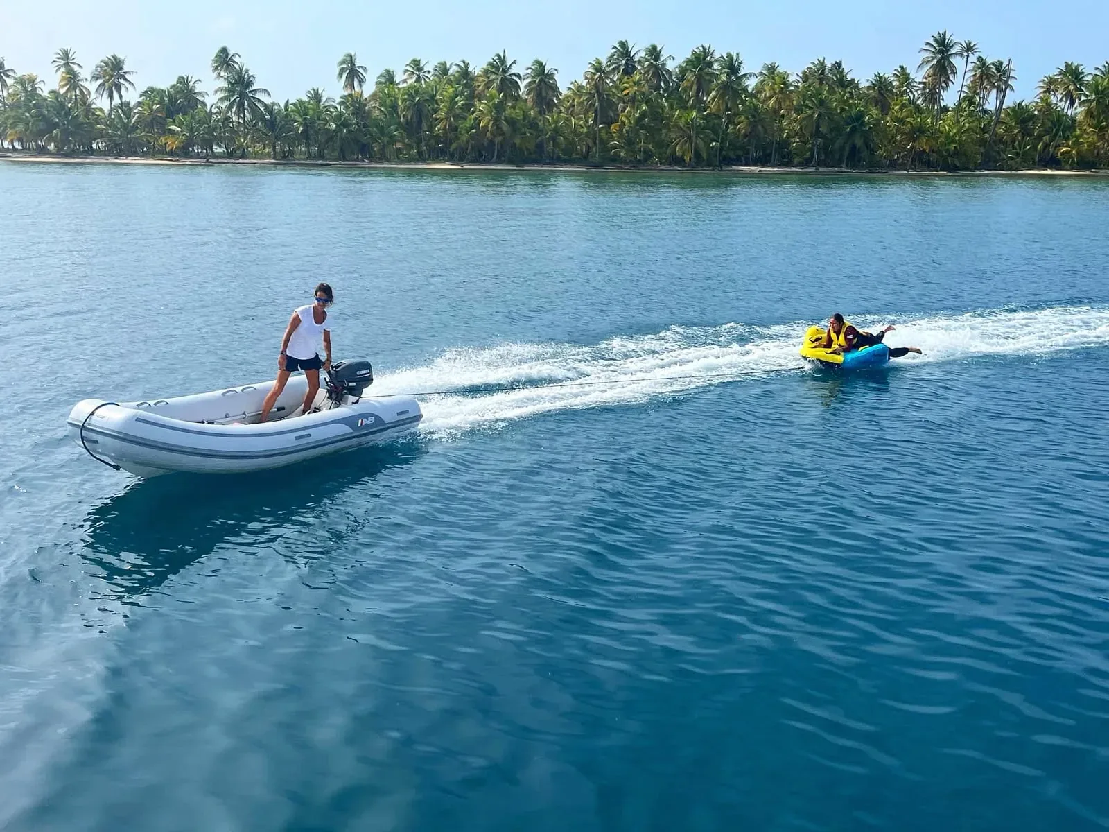 Dinghy from the Lagoon 55 towing guests on an inflatable towable past a palm shoreline