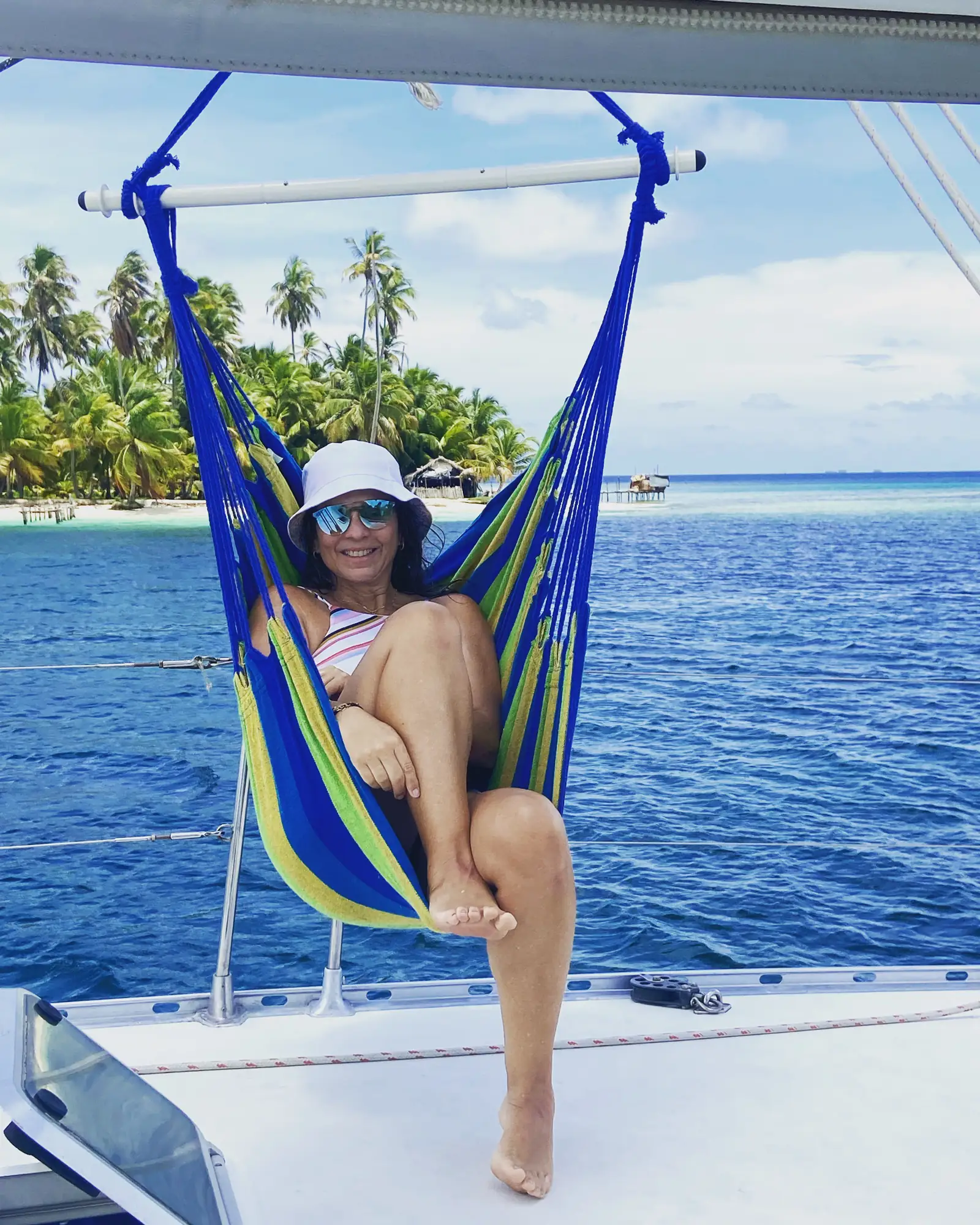 Guest relaxing in a hanging hammock chair off the side of the Lagoon 55, palm island behind