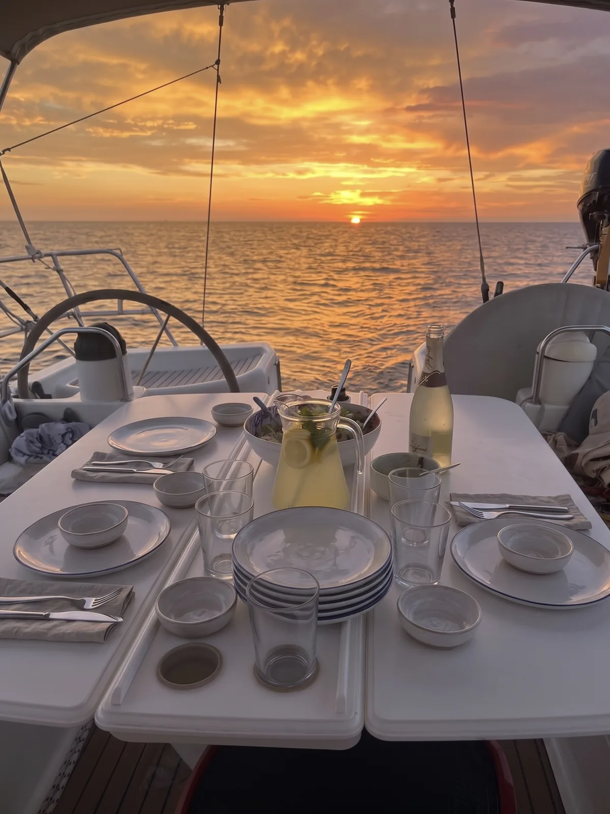 Cockpit table set for dinner at sunset with a jug of lemonade