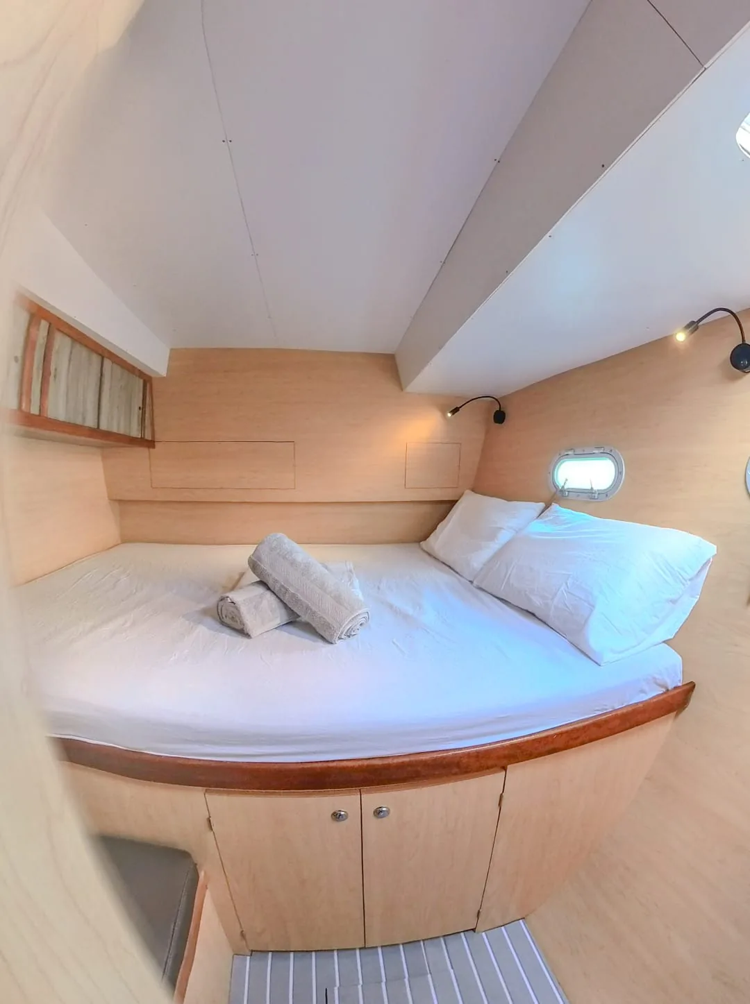Double cabin with a made-up bed, rolled towels and a porthole