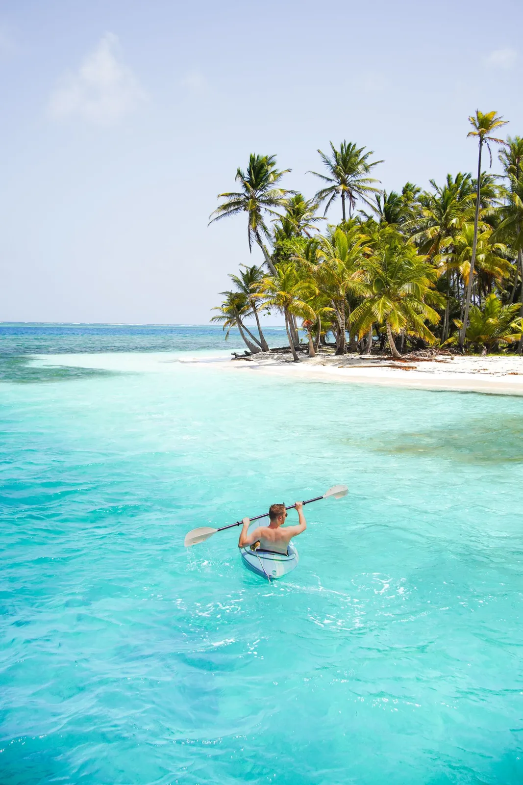 A kayaker in shallow turquoise water off a palm island