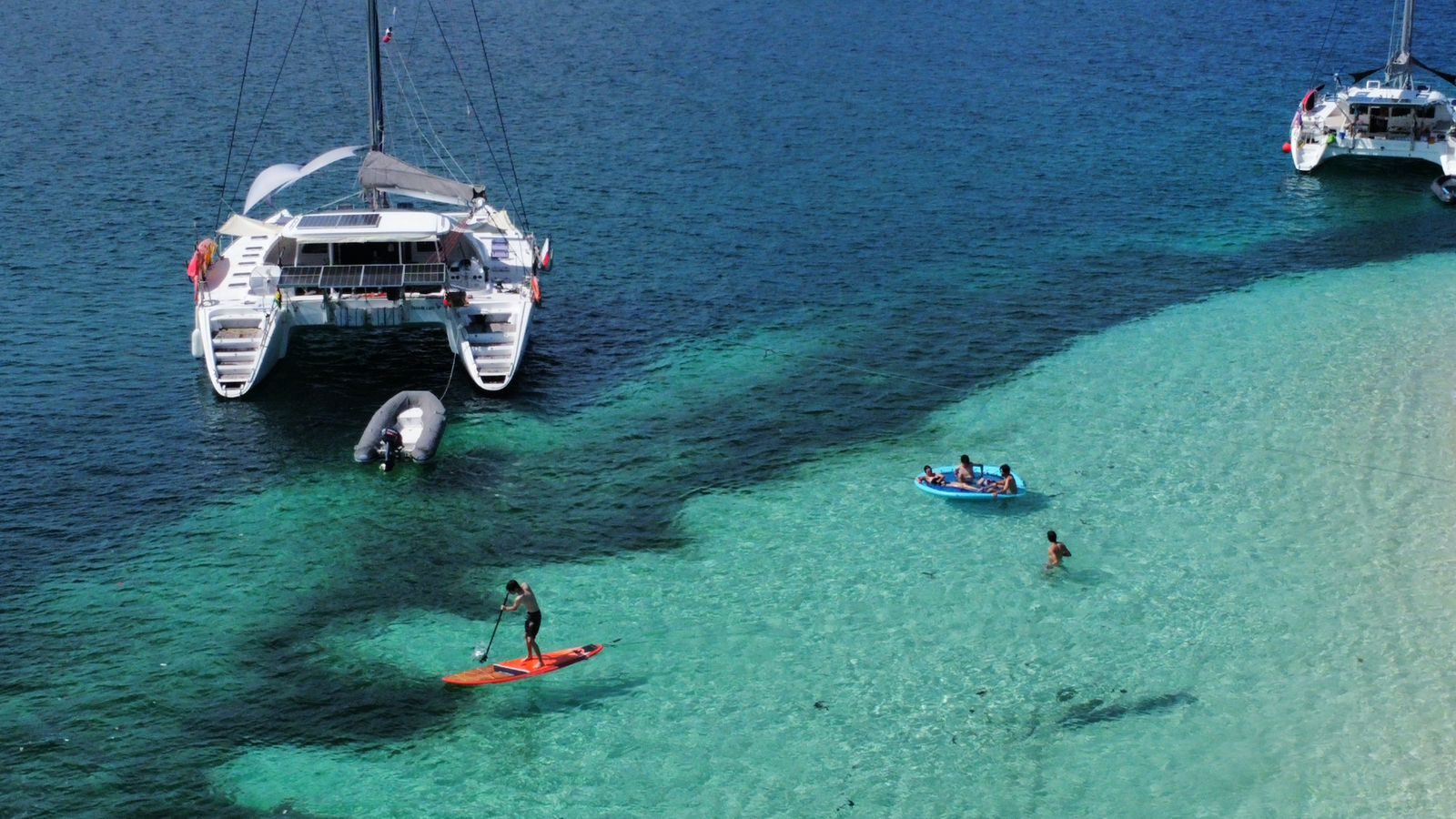 Aerial view of the catamaran at anchor with guests swimming and paddleboarding