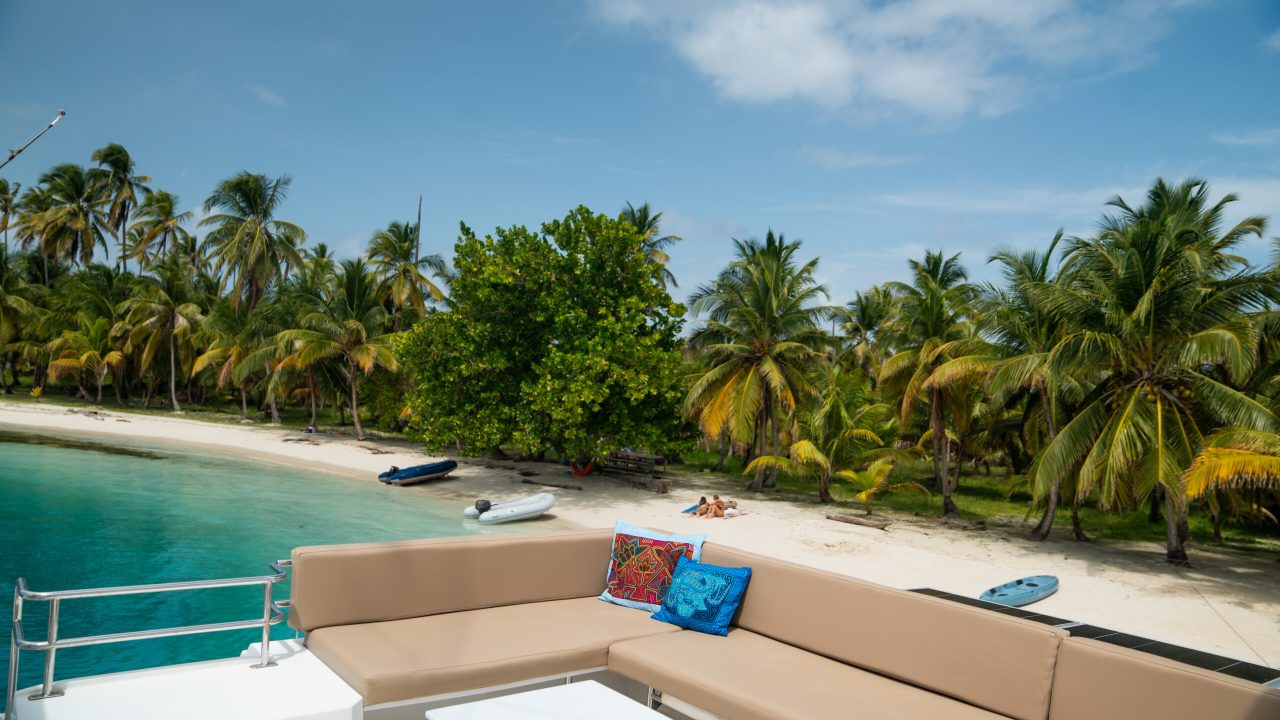 View from the deck of a luxury sailing catamaran in San Blas, Panama, showing crystal-clear water, palm trees, and white sandy beaches.
