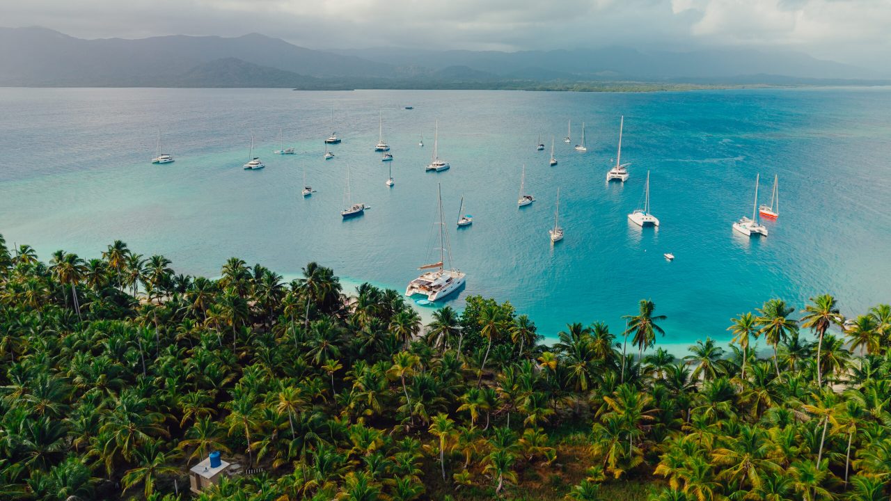 Aerial photo of multiple sailboats anchored off the lush green islands of San Blas, Panama, surrounded by turquoise Caribbean waters.